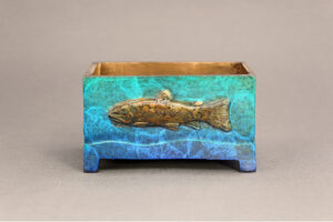 Small bronze box with a trout relief on either side.