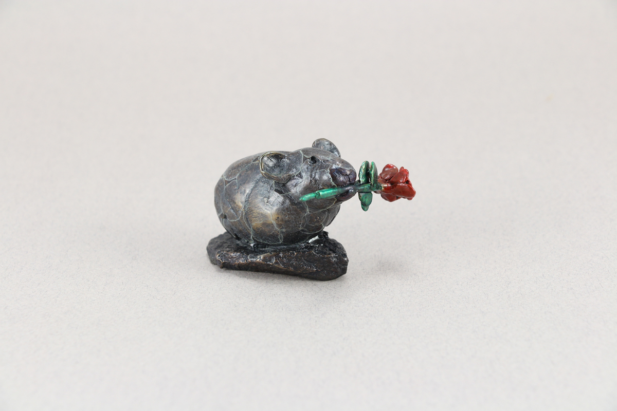 Small little bronze Pika with a flower in it's mouth.