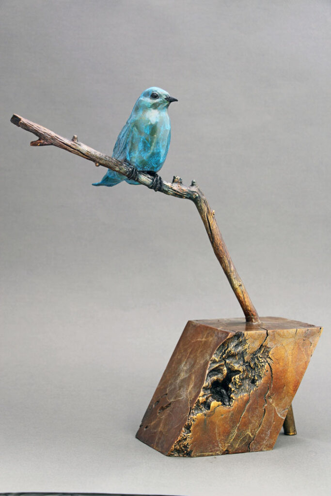 This bronze sculpture depicts a Bluebird sitting on a branch. The base was formed from the burl of a piece of scrub oak