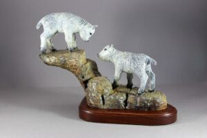 Bronze sculpture of two playful baby mountain goats on rocky ledge engaged in a stare down.